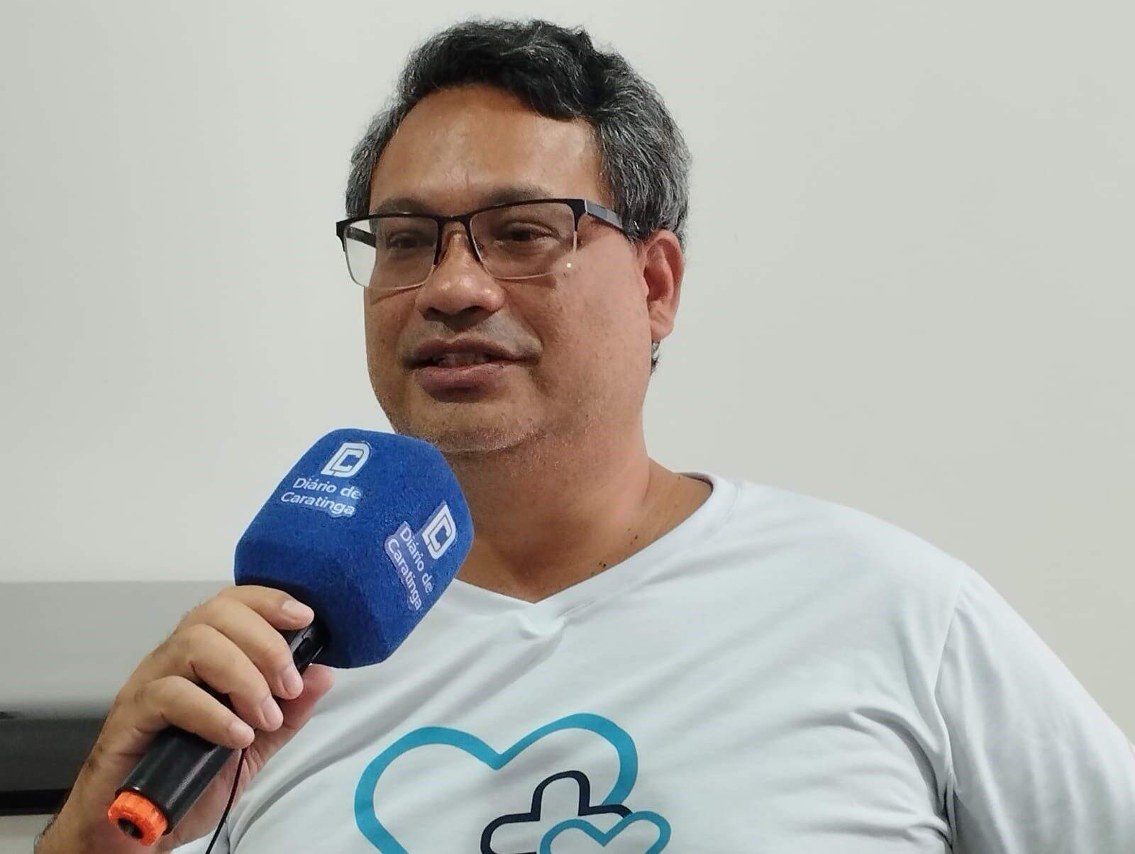 Man speaking into a blue branded microphone, wearing a t-shirt with a blue heart logo